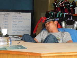 Nim Bahadur Magar asleep behind the desk at Paddle Nepal’s early operations office in Pokhara after long days balancing guiding, competitions, and running the growing business.