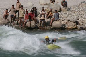 Nim Bahadur Magar surfing a standing wave on the Sun Koshi River while local villagers watch from the riverbank during an expedition in eastern Nepal.