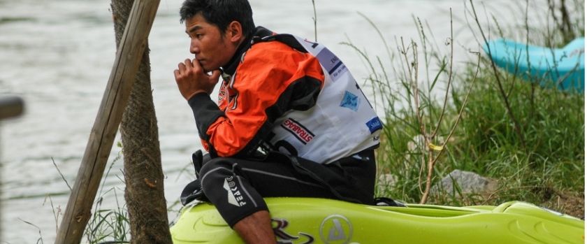 Nim Bahadur Magar sitting on the front of a kayak by a river in Europe, quietly reflecting during a paddling journey in 2003.